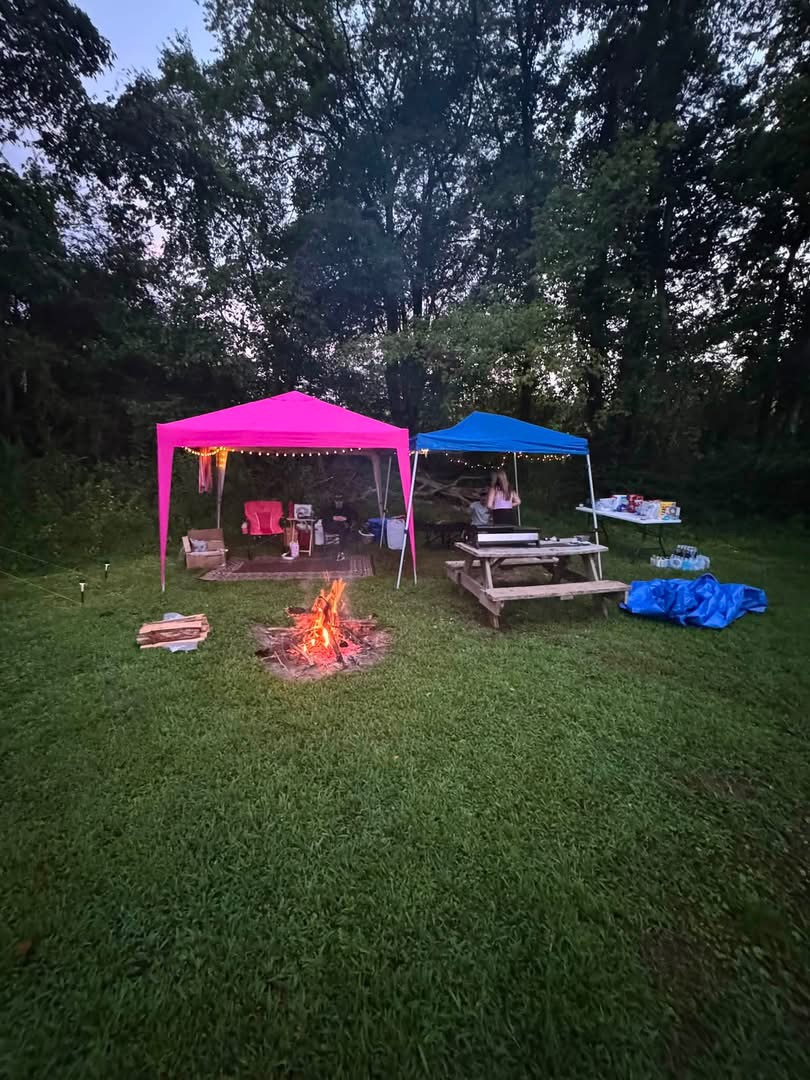 Two canopies and a fire ring at a grassy campsite at dusk
