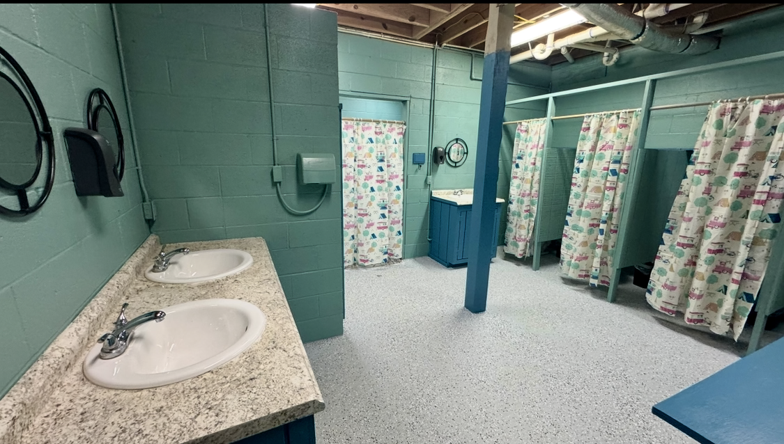 Interior of the main shower house at Crazy Horse with several curtained shower stalls and double sinks