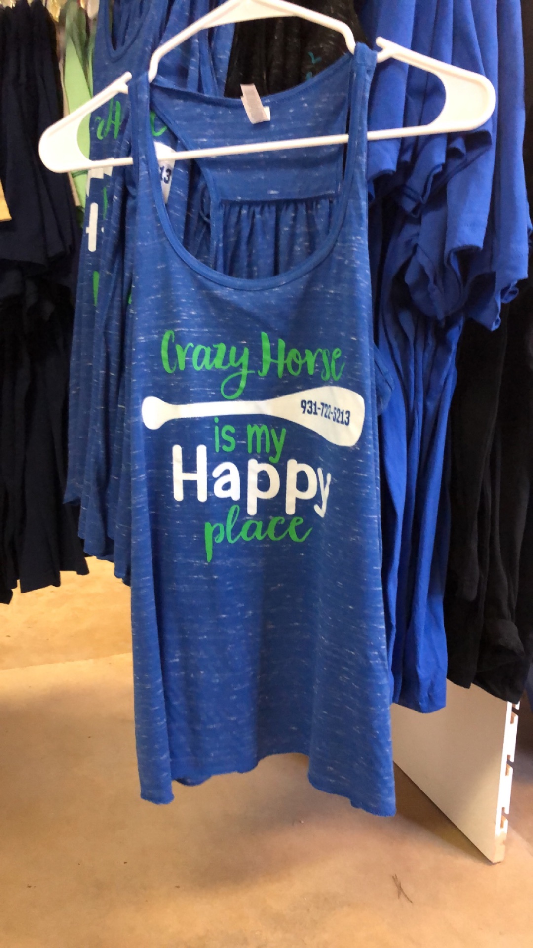 A blue Crazy Horse is my Happy Place tank top on a hanger