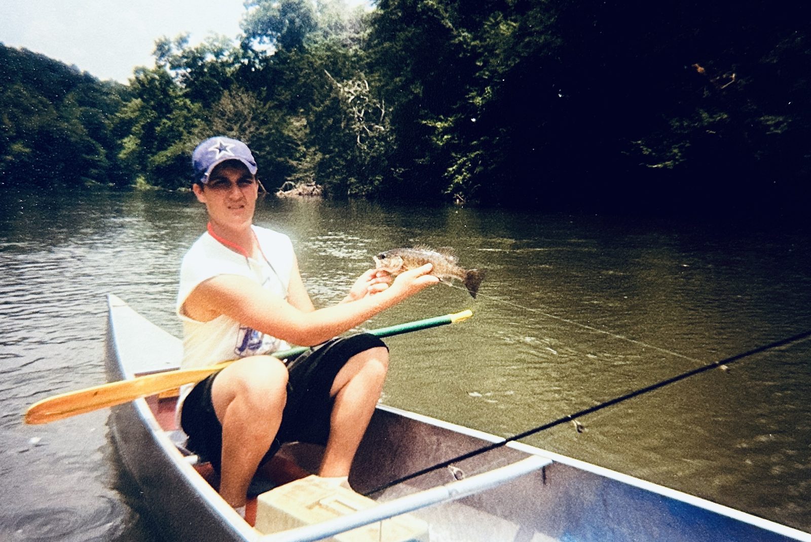 A young paddler holding up a smallmouth bass from the bow of a canoe