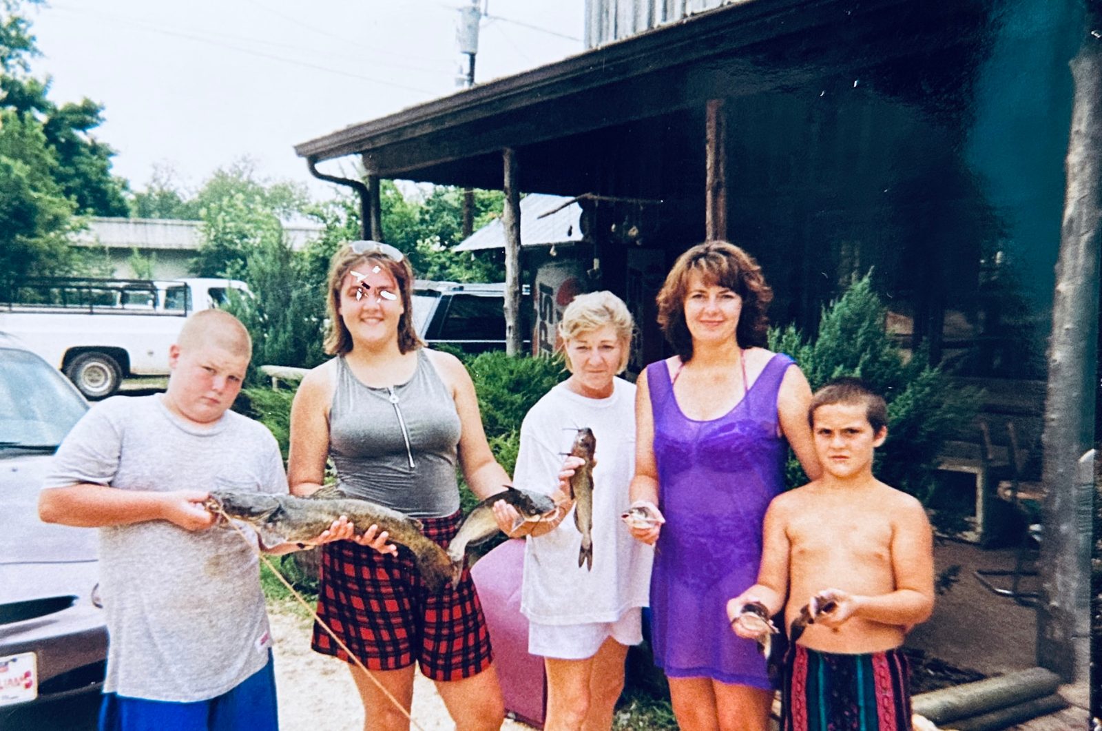 Family and campers holding up a stringer of catfish in front of the old office