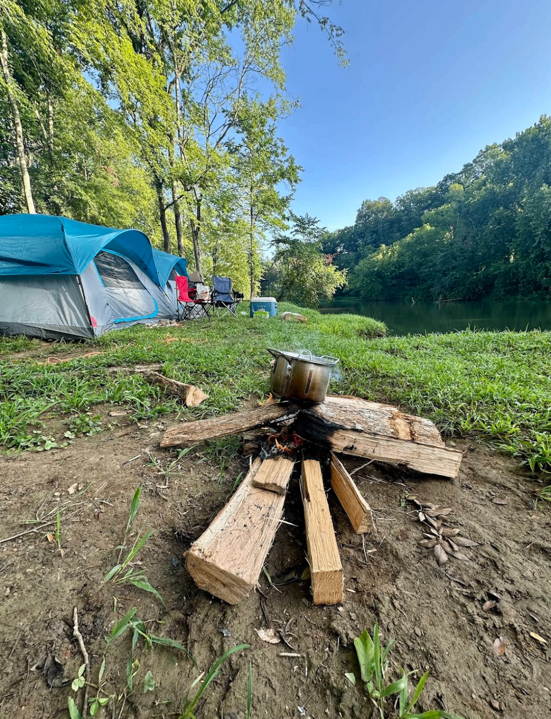 Campfire with a coffee pot beside tents on the Buffalo River bank
