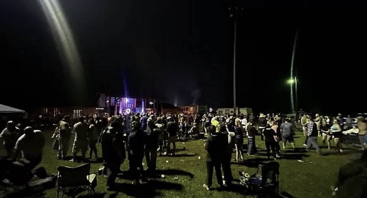 Crowd filling the field in front of the lit stage on an event night