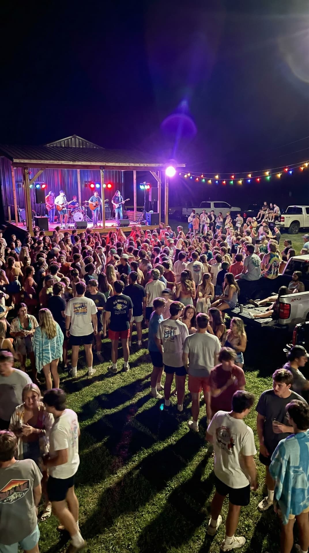Band playing on the stage at night with the crowd on the grass