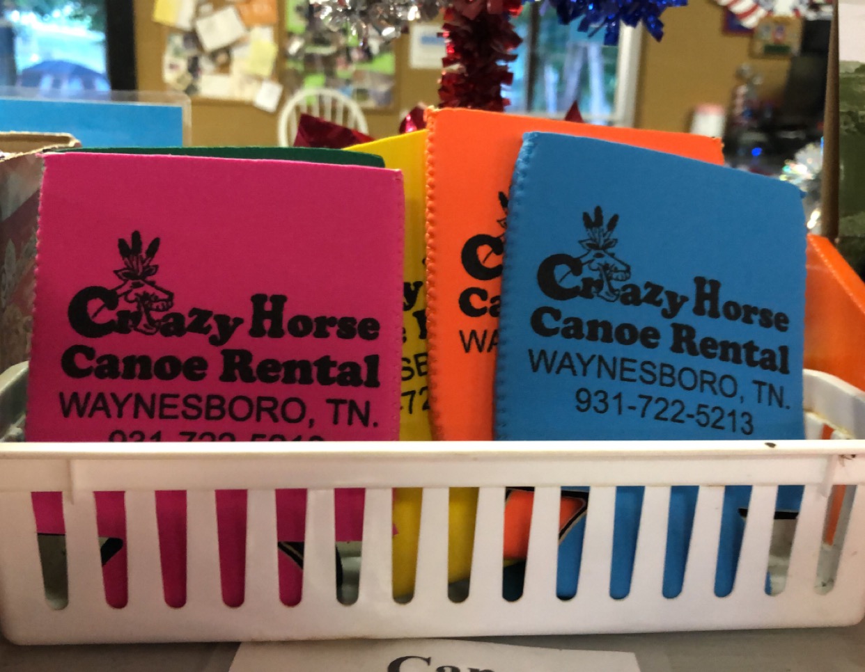 Bright flat Crazy Horse Canoe Rental koozies in a basket