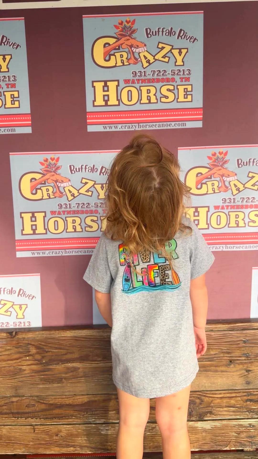 Little girl showing off a River Life t-shirt from the camp store